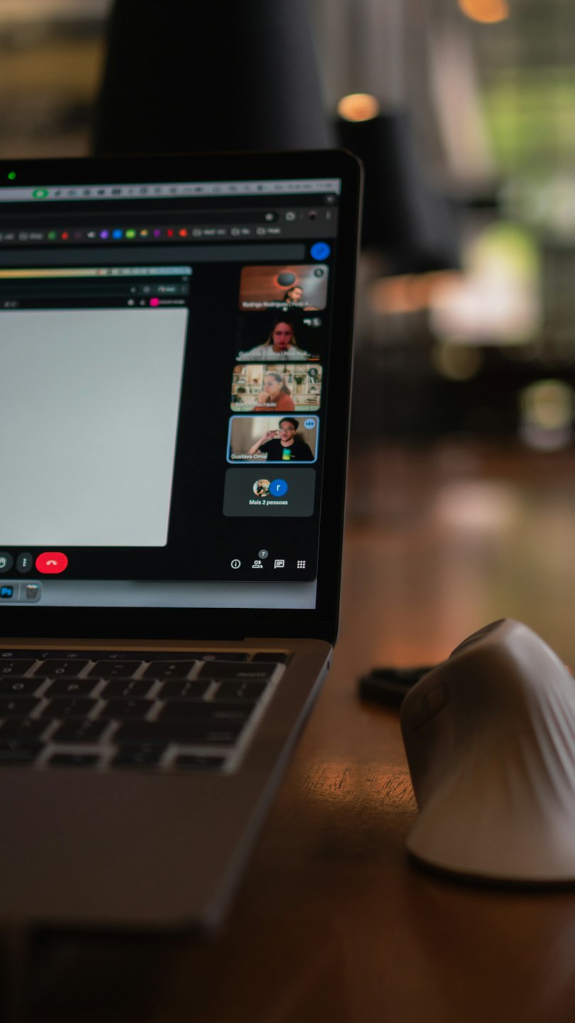 Laptop che mostra una videoconferenza su una scrivania di legno.