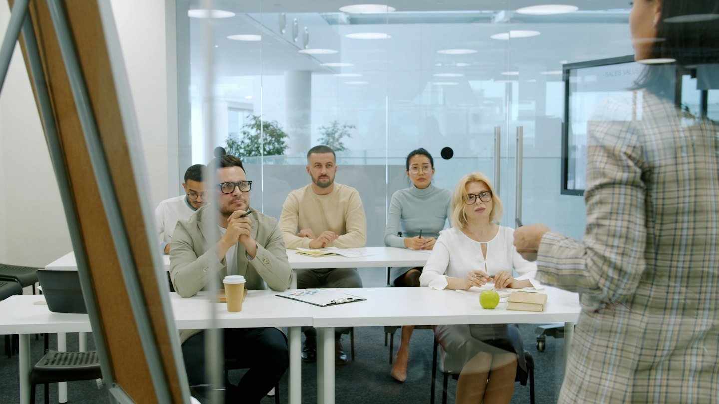 Professionisti diversi ascoltano un relatore in una moderna sala conferenze.